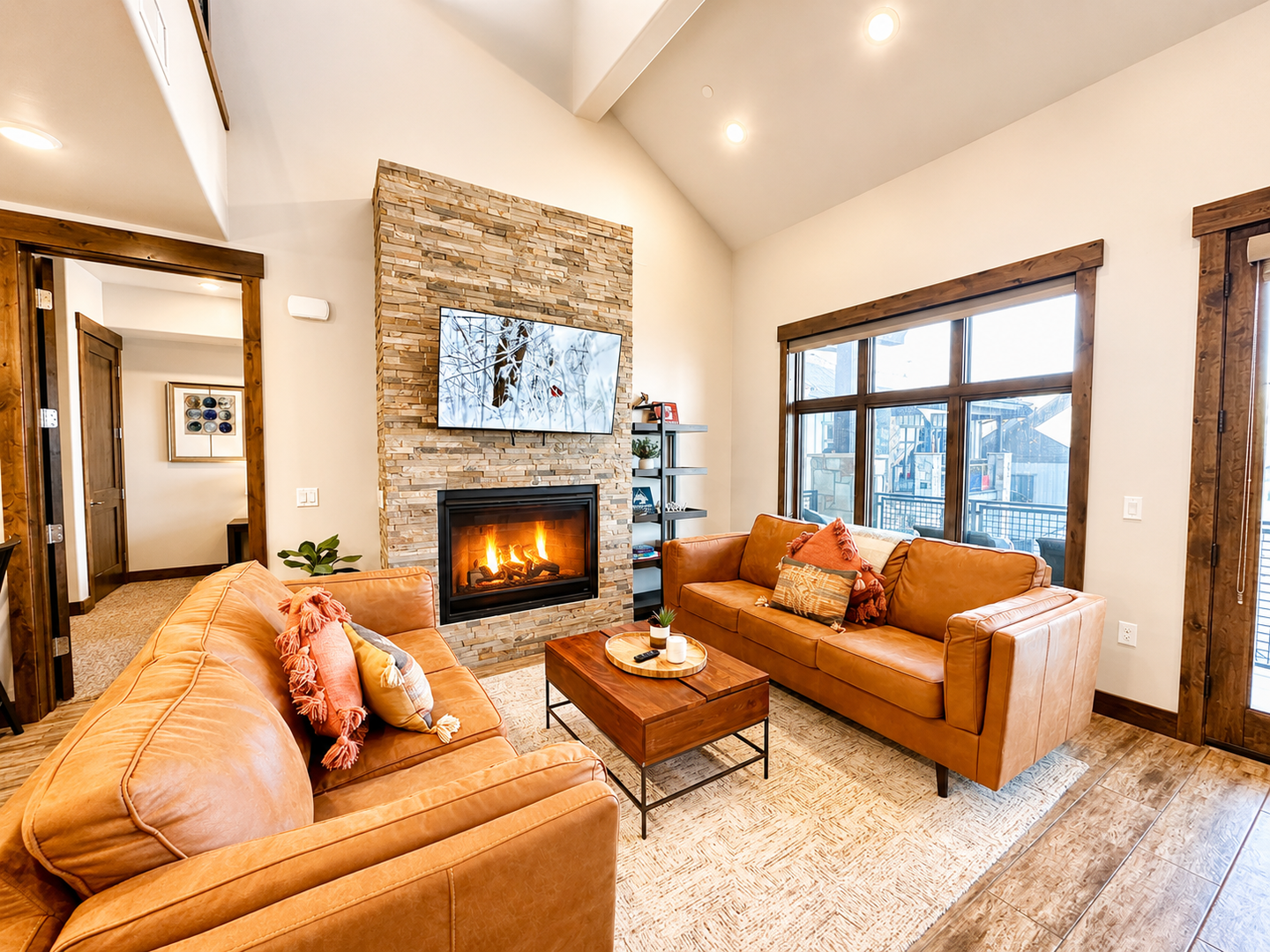 Relax in this luxurious open-concept living area. It features a stunning floor-to-ceiling stone fireplace, plush leather seating, and a modern kitchen with high-end finishes, perfect for mountain getaways.