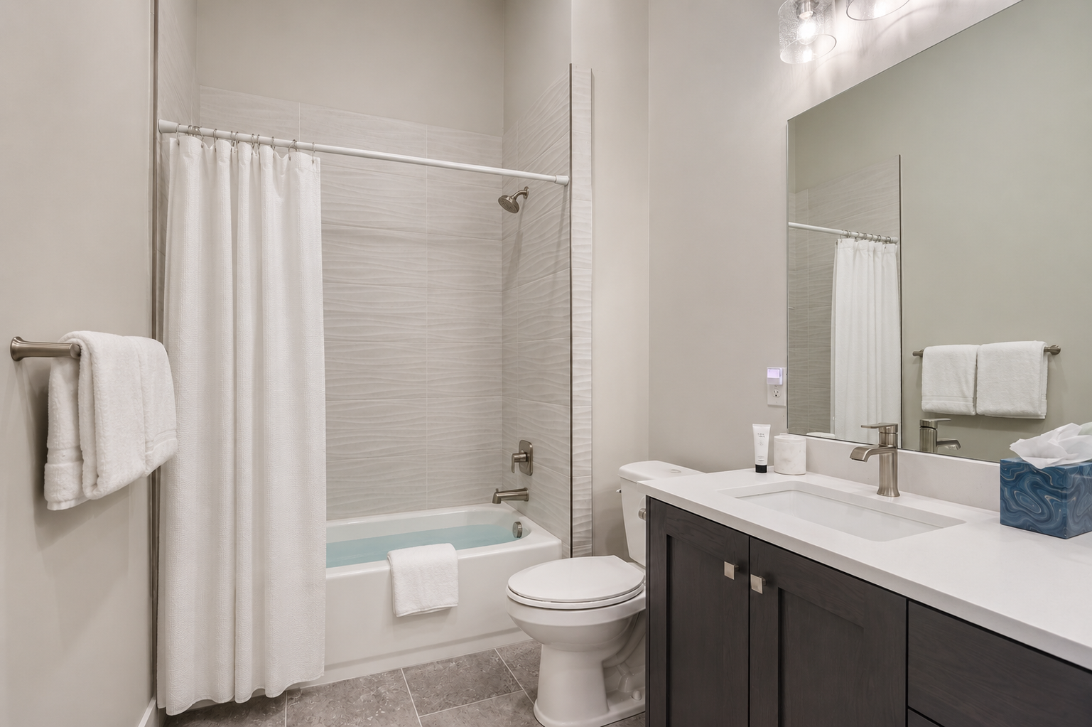 Refresh in your modern, pristine bathroom with soothing tiled tub, sleek vanity, and plush towels awaiting your arrival.