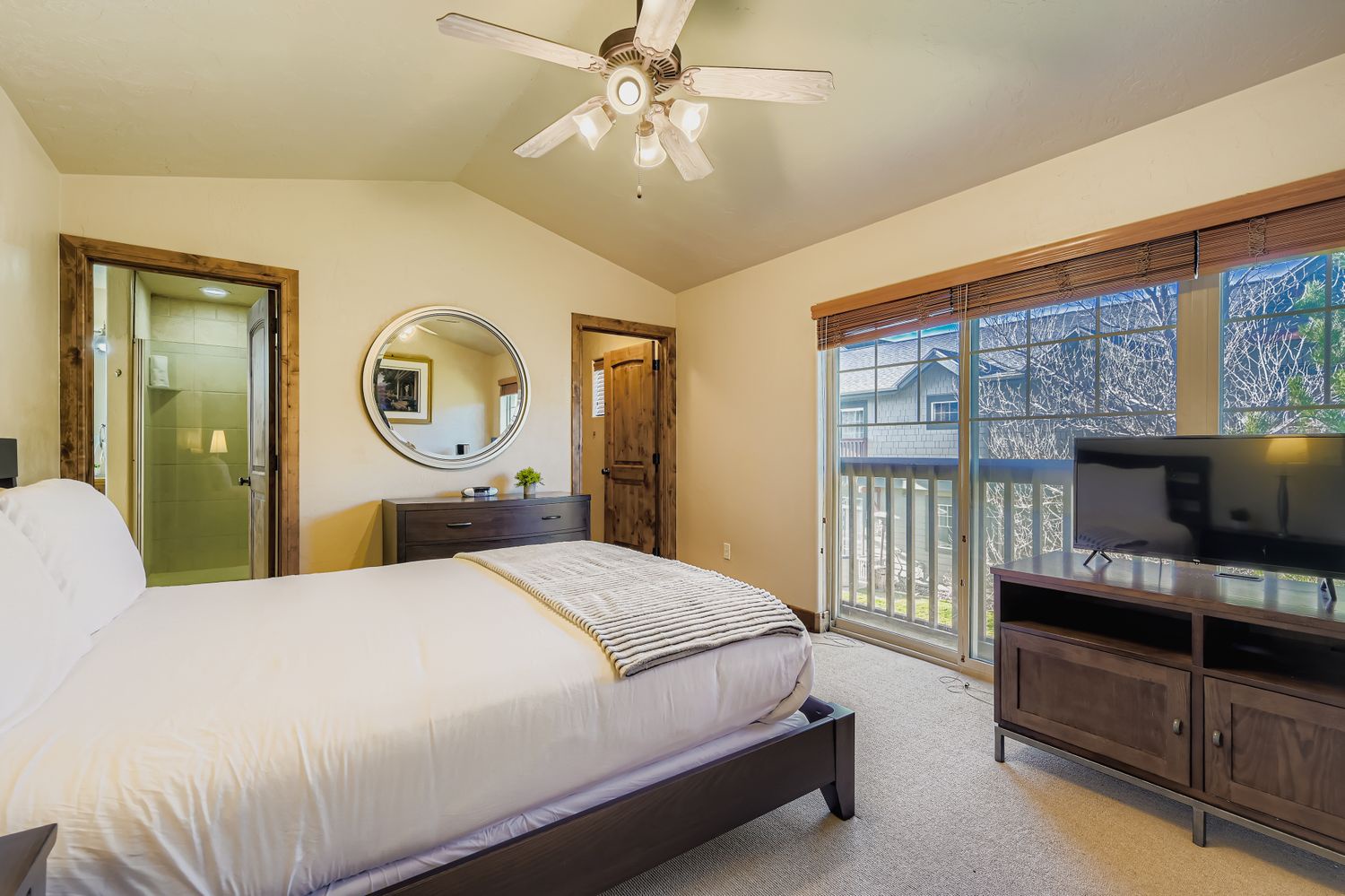 Relax in your spacious bedroom featuring a comfortable bed, entertainment center, and private access to outdoor views through sliding glass doors.