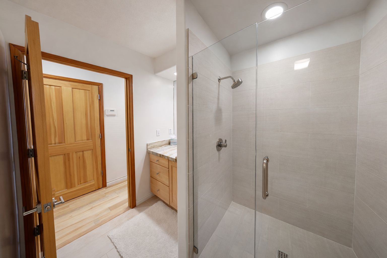 This modern bathroom features a spacious vanity with elegant granite countertops, a large illuminated mirror, and a sleek, glass-enclosed shower for your convenience.