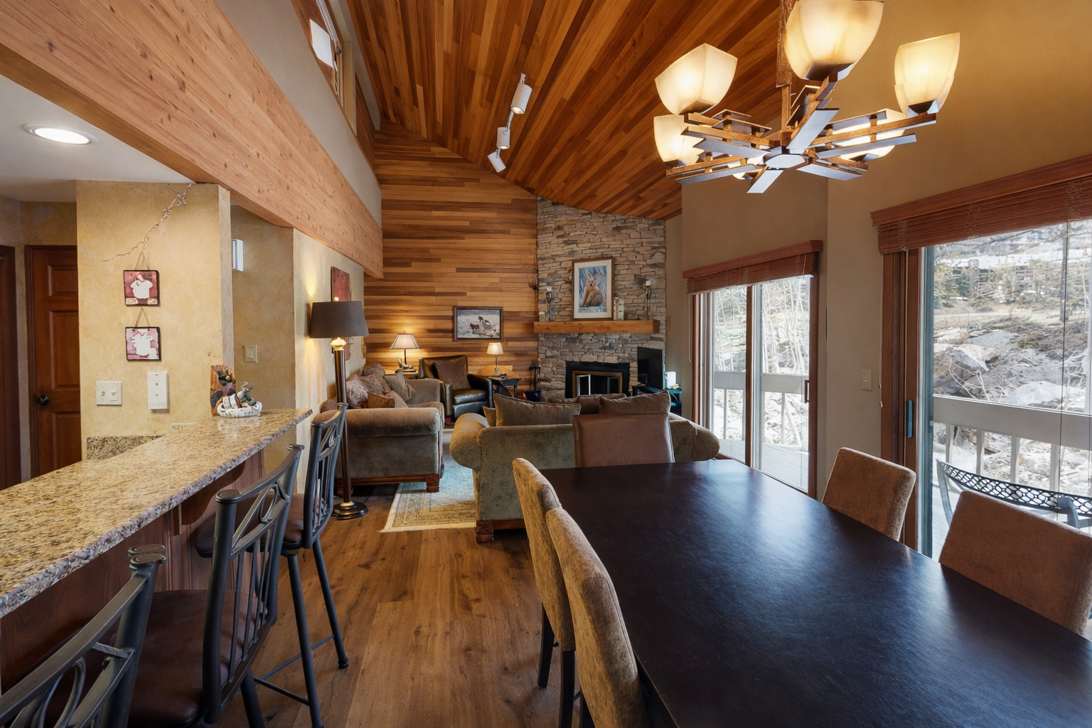 A stunning open-concept living space greets you with soaring wood-paneled ceilings, a cozy stone fireplace, and expansive windows framing peaceful mountain views—your perfect alpine retreat.