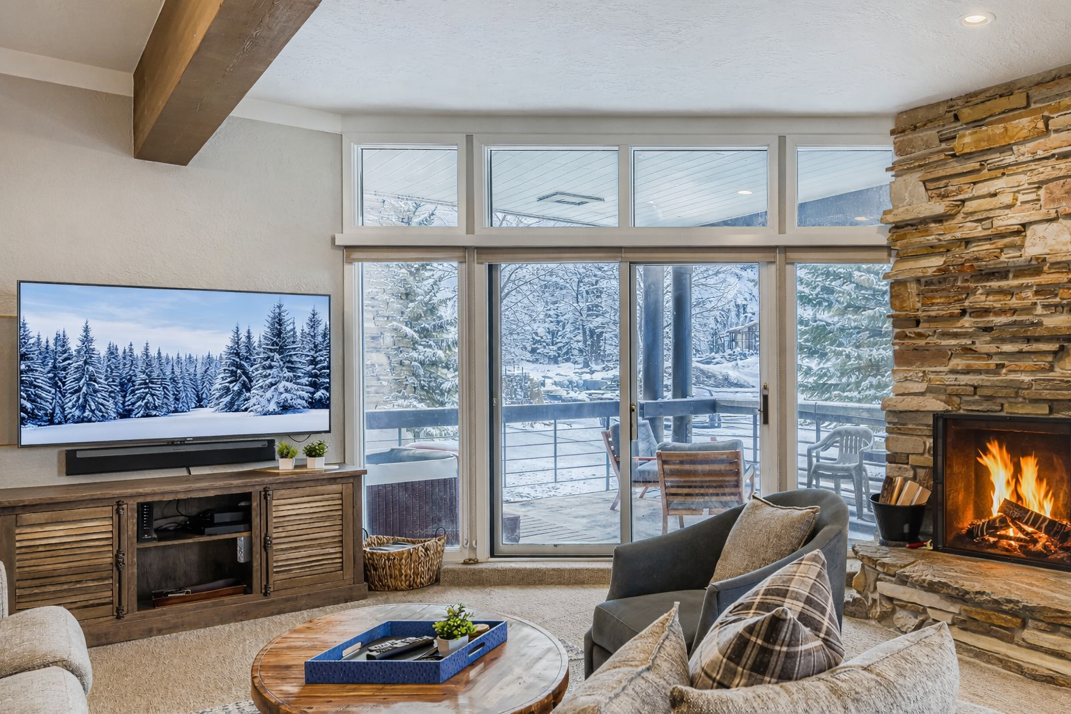 Unwind in your cozy living room featuring exposed beams, stone fireplace, and large windows that frame peaceful mountain views - the perfect retreat after a day of adventure.