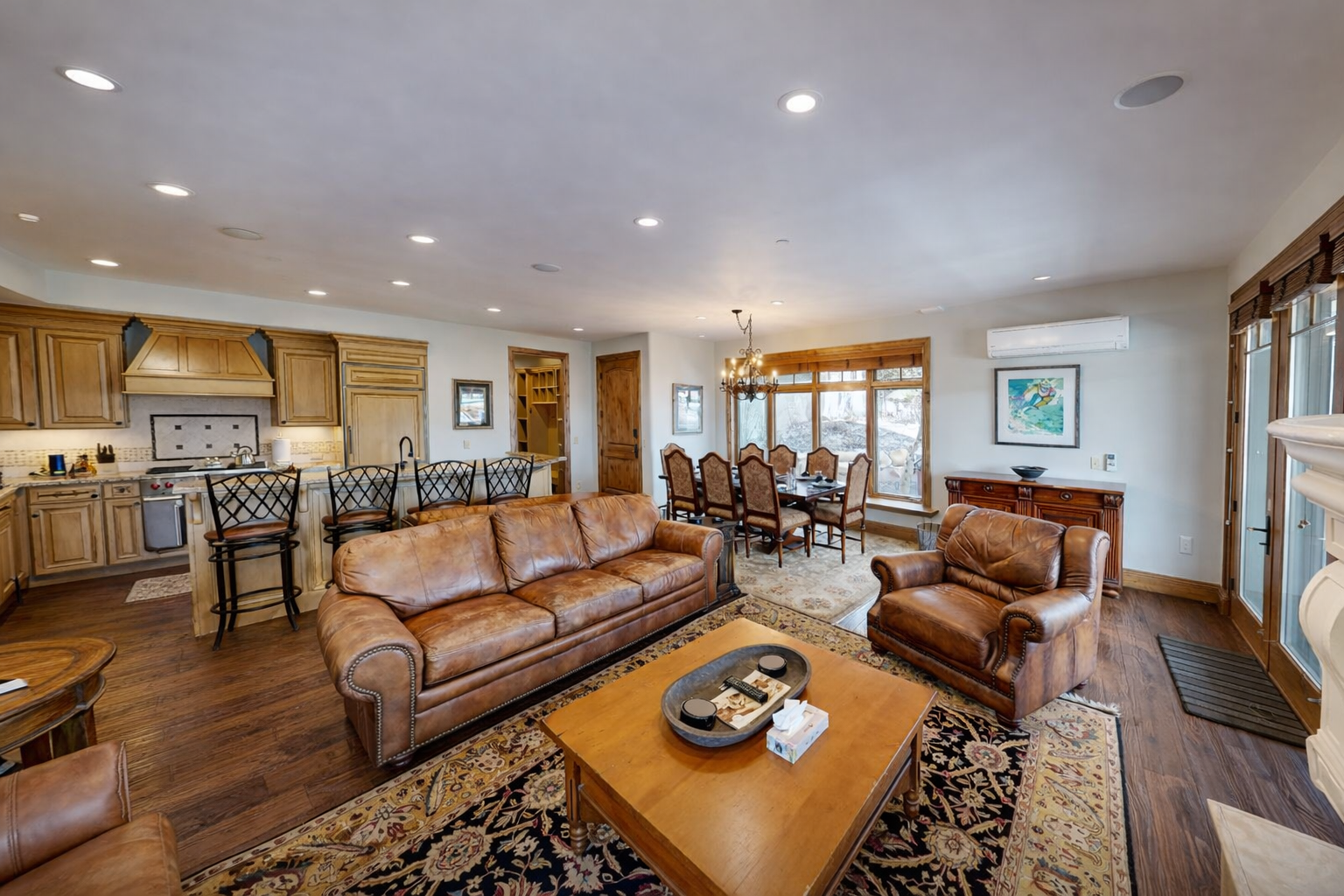 Relax in this bright, open-concept living area at Strand Haus, featuring plush leather seating, a cozy gas fireplace, and a large smart TV.