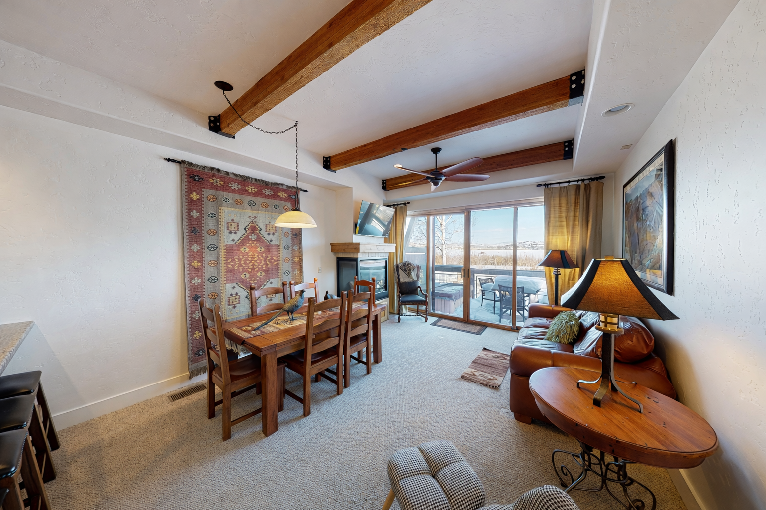 Gather around the rustic dining table under exposed wooden beams, where sunlight streams in through expansive windows. Your cozy retreat features a warm fireplace and opens to a private balcony with stunning views.