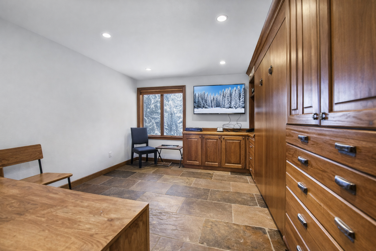 Cozy multi-use room featuring extensive wood cabinetry, stone flooring, and a large TV. A quiet, comfortable space perfect for work or relaxation during your mountain escape.