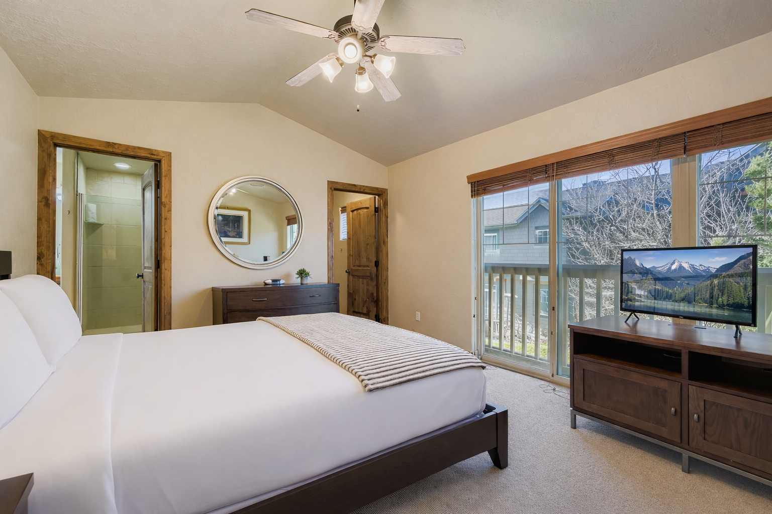 Relax in your spacious bedroom featuring a comfortable bed, entertainment center, and private access to outdoor views through sliding glass doors.