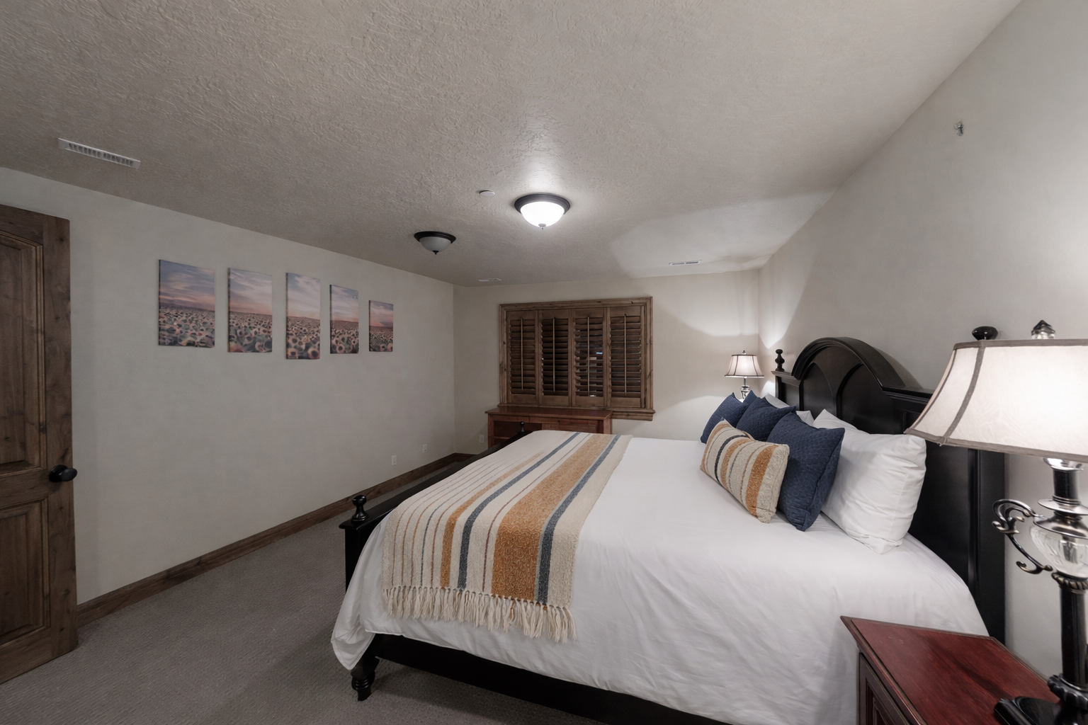 This spacious guest room features a grand four-poster bed, premium linens, and warm bedside lighting. Shuttered windows and plush carpeting create a quiet, comfortable retreat for a restful night.