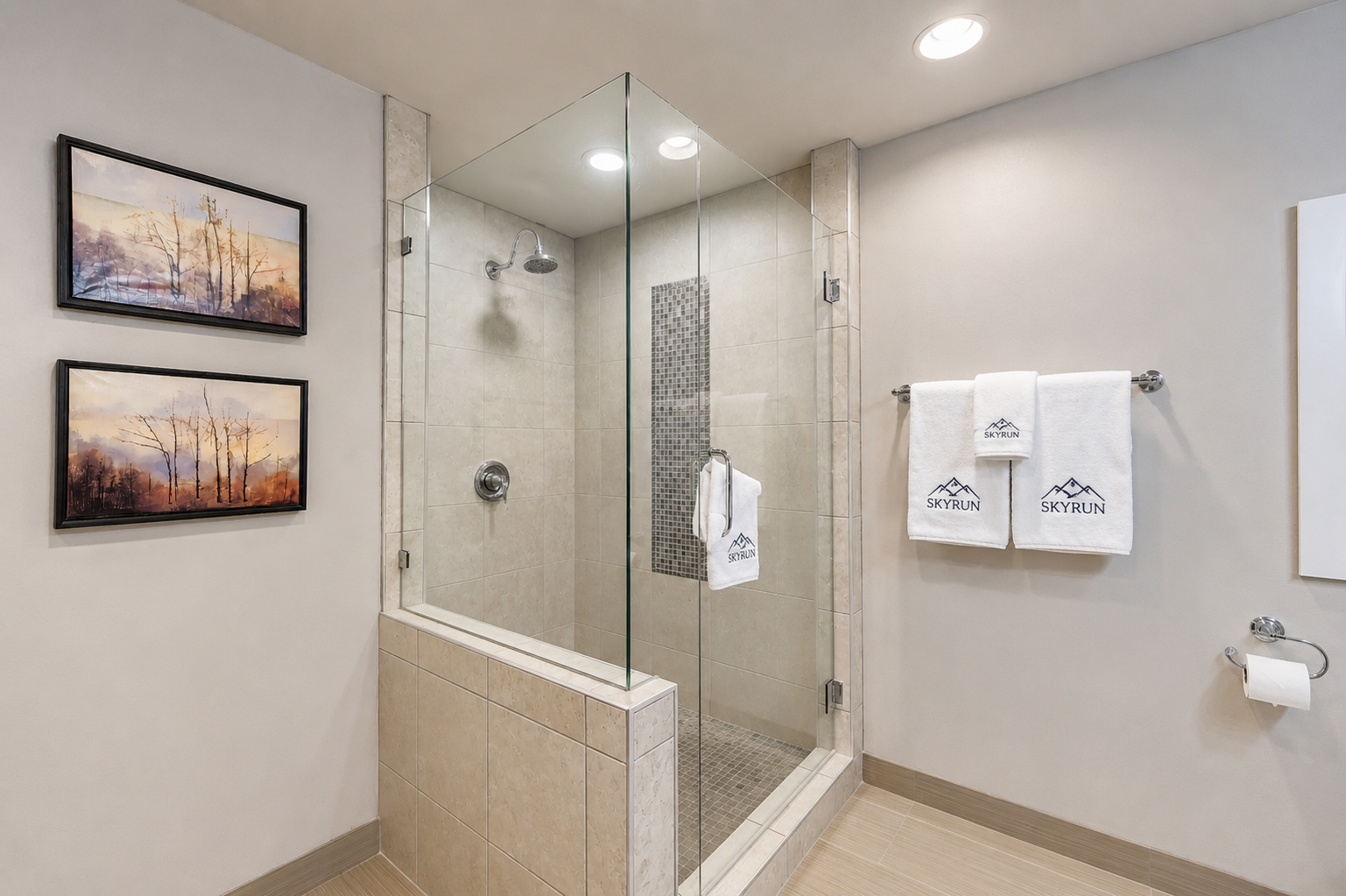 Your modern bathroom features a spacious glass-enclosed walk-in shower with rainfall showerhead, plush branded towels, and serene artwork creating a spa-like retreat for your mountain getaway.