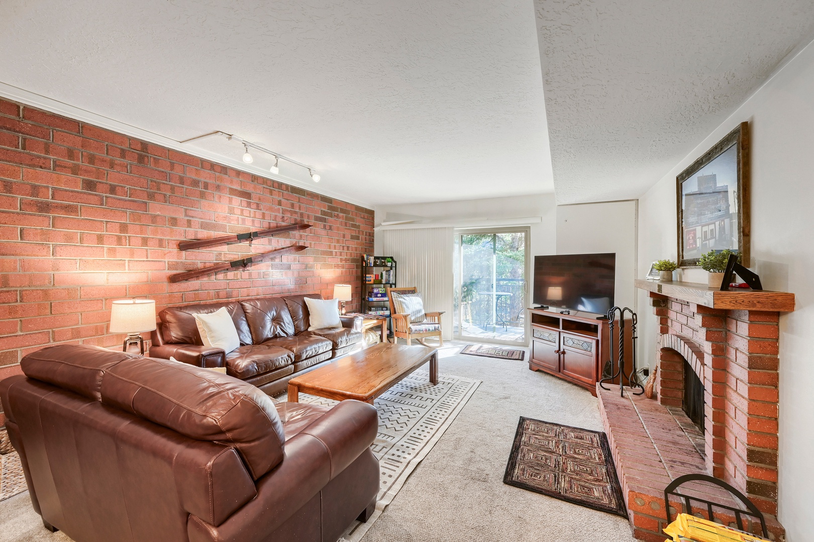 Relax in your inviting living room featuring warm leather seating, a cozy fireplace, and natural light streaming through the patio door, creating the perfect retreat after your day's adventures.