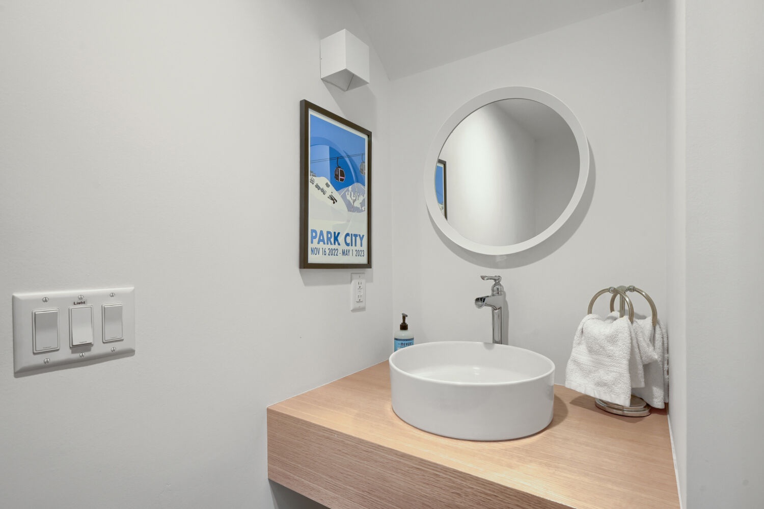 Freshen up in this sleek, modern bathroom featuring a vessel sink atop warm wood, a chic circular mirror, and crisp white towels ready for your arrival.