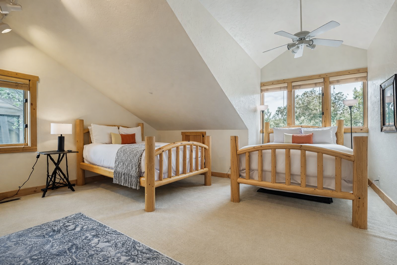 Cozy up in your bright attic bedroom featuring twin beds with rustic wooden frames and peaceful tree views.