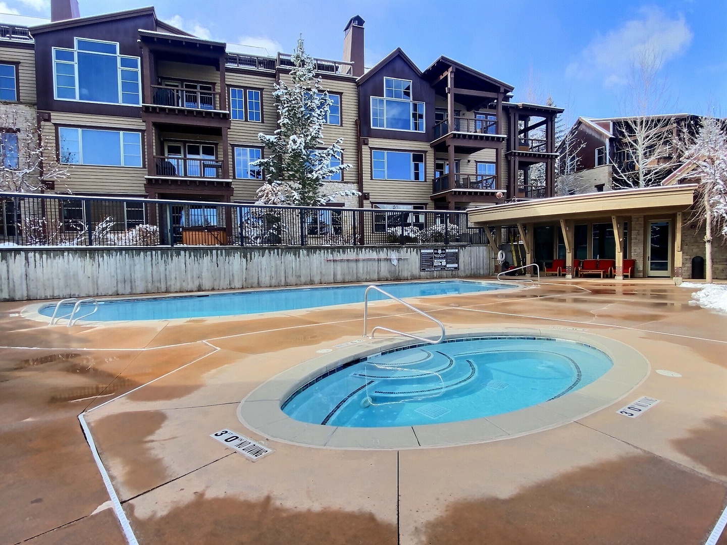 The property features an outdoor pool and hot tub surrounded by a spacious deck area, with mountain architecture providing a scenic backdrop.