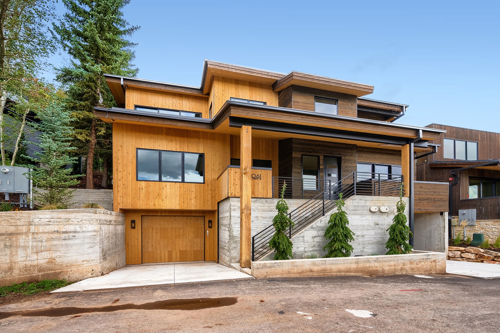 A striking modern mountain home with natural wood siding and contemporary architecture, set among towering pines in a peaceful wooded neighborhood.