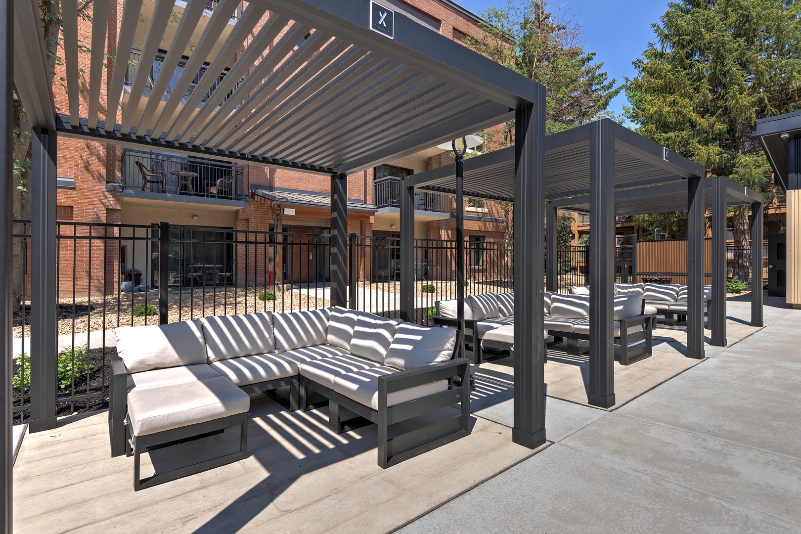 Modern louvered cabanas with plush daybeds create perfect spots to lounge under the shade. These outdoor retreats combine comfort and contemporary design in a peaceful courtyard setting.