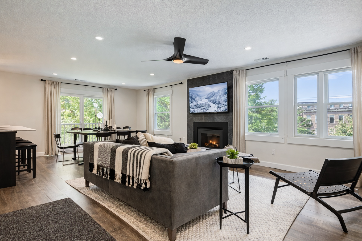 Relax in your spacious living room featuring a cozy fireplace, modern furnishings, and abundant natural light from large windows overlooking the neighborhood.