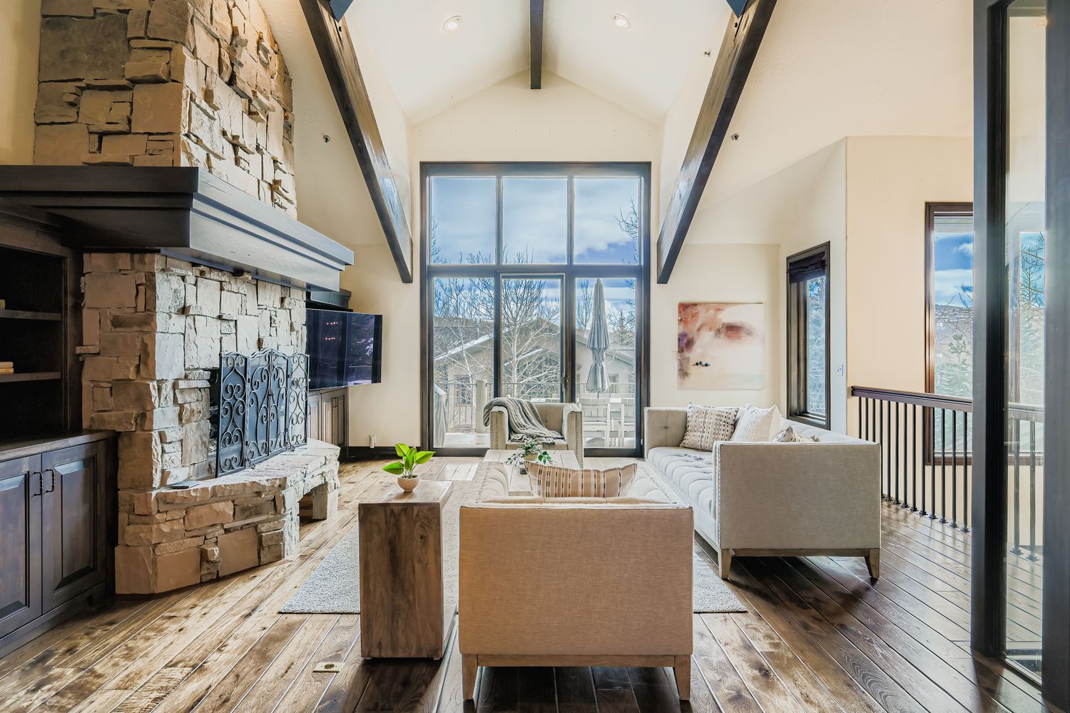 Relax in your elegant living space featuring a stunning stone fireplace, soaring vaulted ceilings with exposed beams, and comfortable seating where you can unwind while enjoying mountain views.