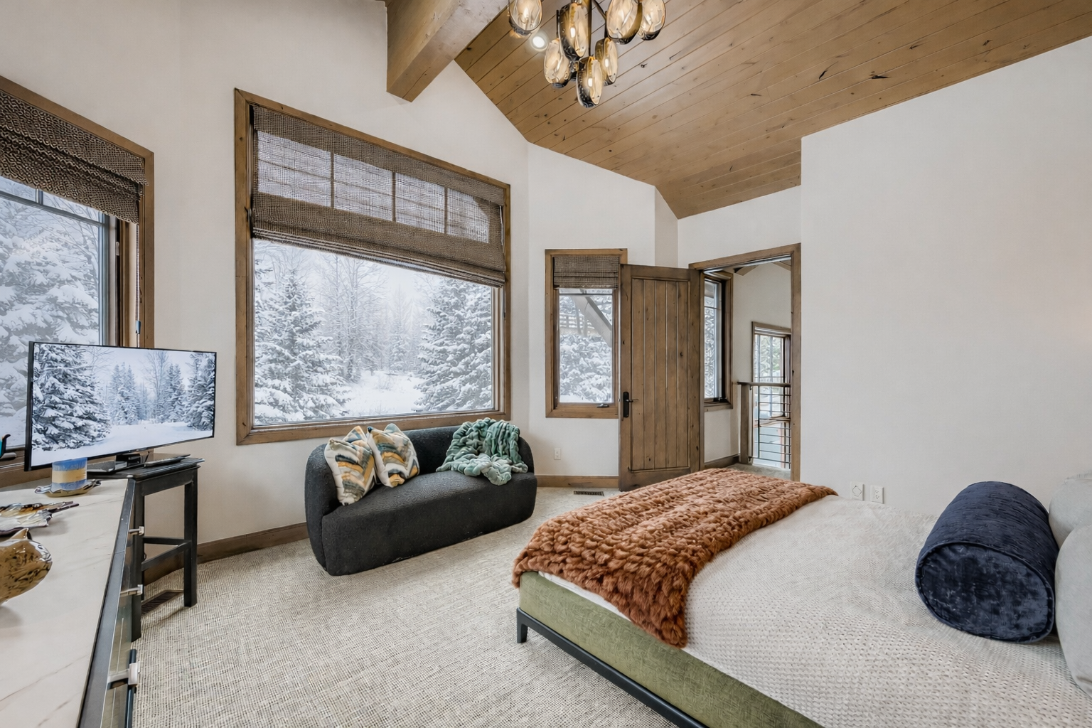 Unwind in your elegantly appointed bedroom featuring exposed wood beams, luxurious bedding, and panoramic mountain views through expansive windows.