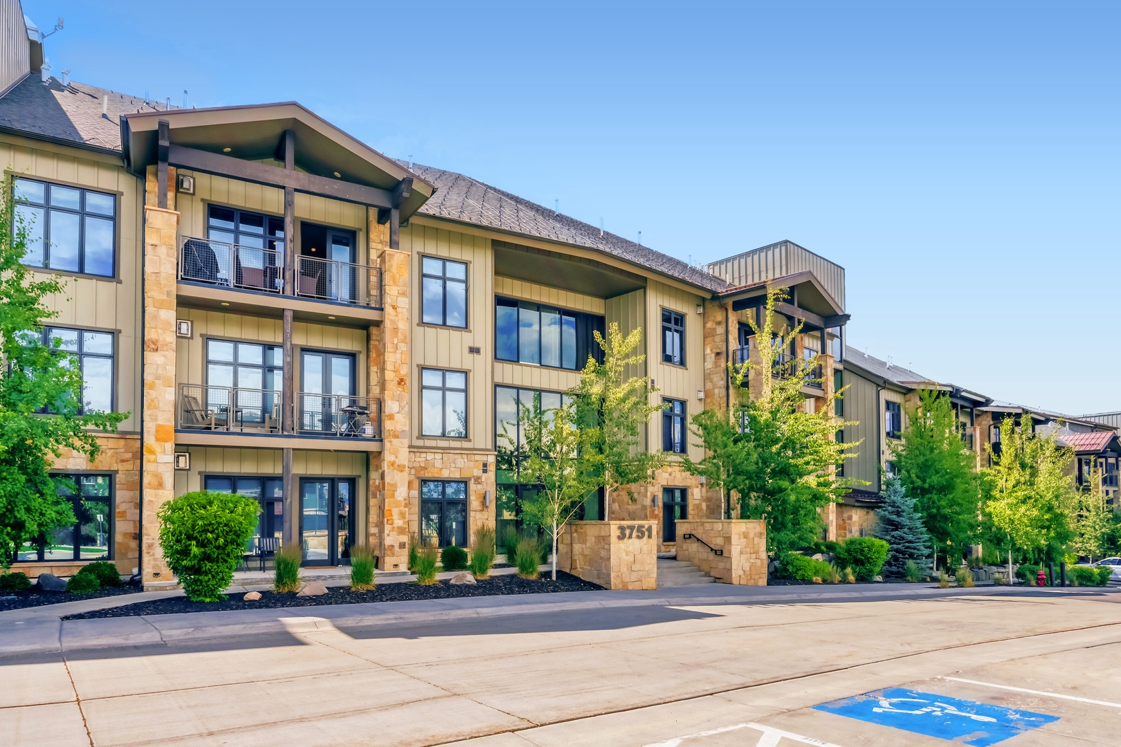 Modern mountain resort building with stone and wood accents, surrounded by landscaped grounds beneath clear blue skies—a welcoming entrance to your vacation retreat.