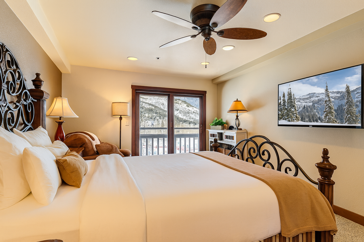 Unwind in this cozy primary bedroom featuring a plush queen bed, warm mountain décor, and a private balcony with beautiful alpine views. Enjoy crisp white linens, soft tan accents, and a comfy reading chair.