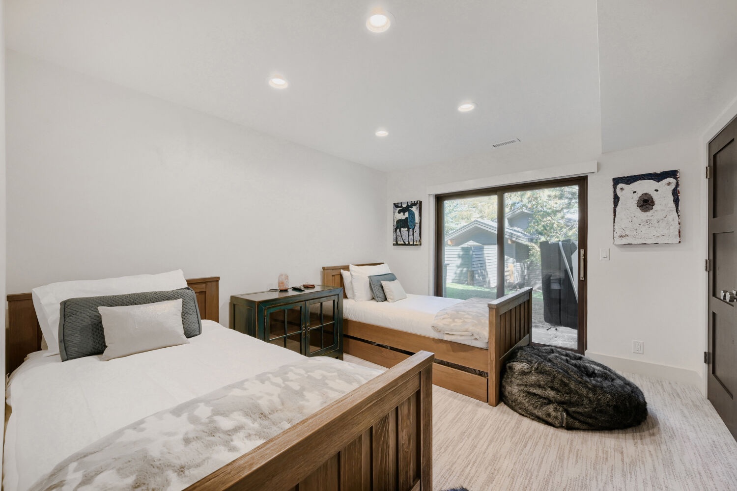 Your bright, welcoming bedroom features two comfortable beds with charming woodland-themed art, soft natural light streaming through a large glass door, and a cozy spot for restful nights.