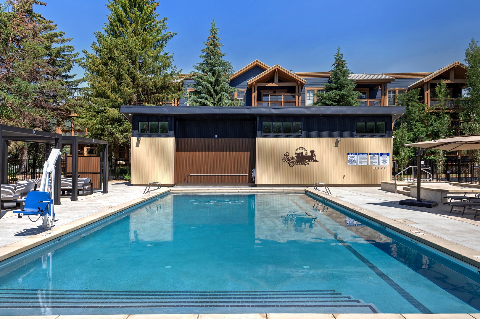 This mountain resort pool area offers a refreshing outdoor swimming space surrounded by towering evergreens and modern amenities, with comfortable lounge seating and a poolside cabana nearby.