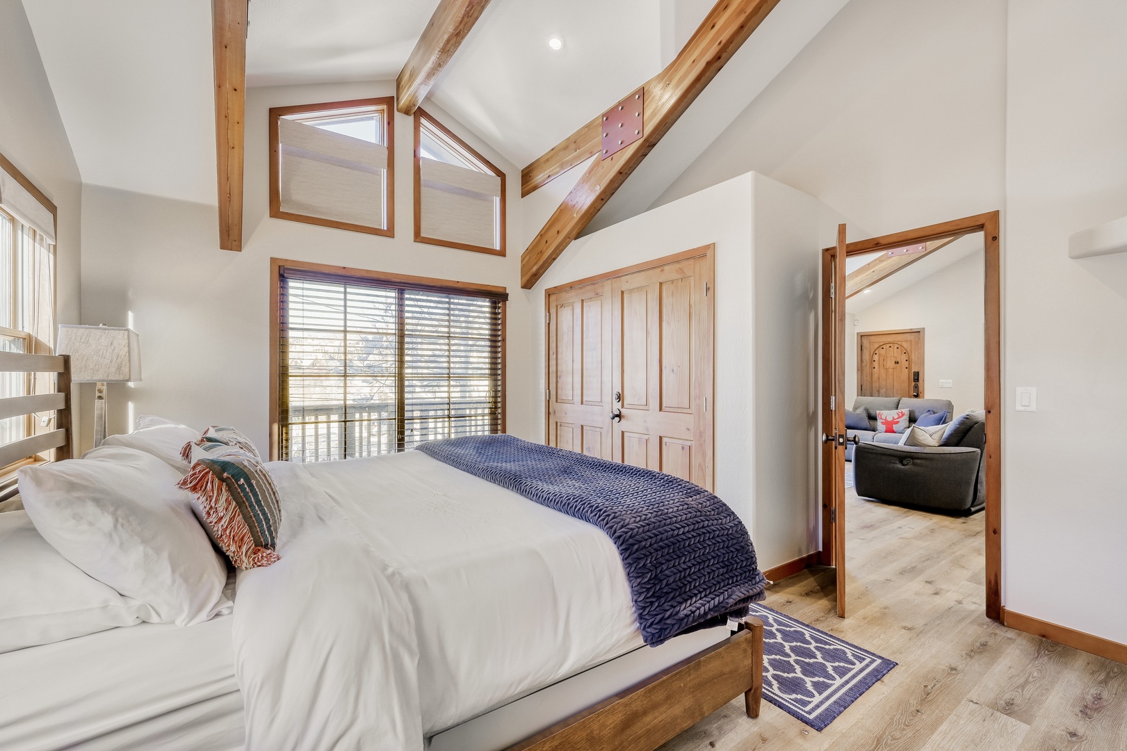 Sink into crisp white linens beneath soaring wooden beams in your serene bedroom sanctuary, where natural light dances through expansive windows.