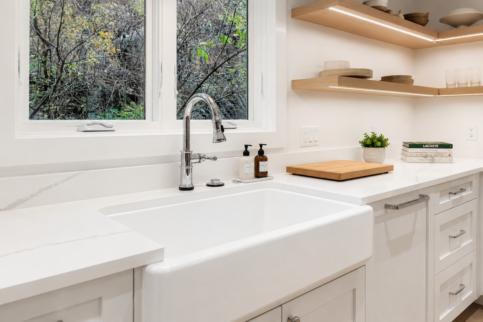 Step into your sleek, modern kitchen with pristine white countertops, open wood shelving, and a farmhouse sink framed by natural light from woodland views.
