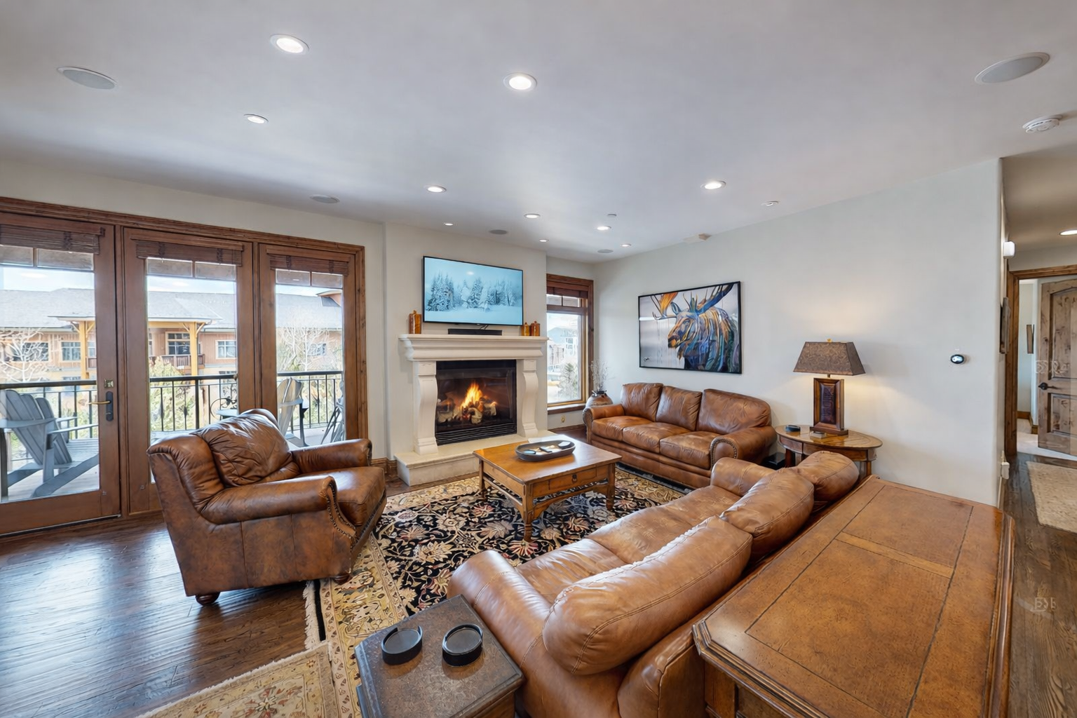 Relax in this bright, open-concept living area at Strand Haus, featuring plush leather seating, a cozy gas fireplace, and a large smart TV.
