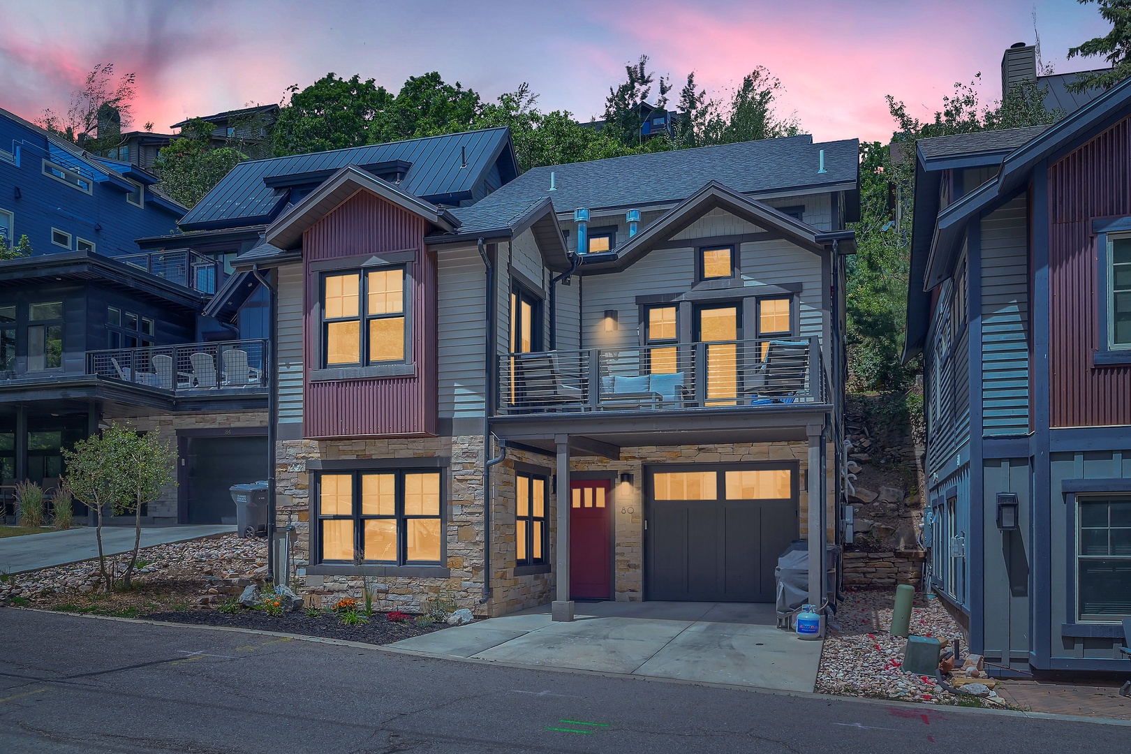 Modern mountain retreat nestled in a scenic neighborhood, featuring contemporary architecture, stone accents, and multiple levels of living space, photographed at twilight with warm interior lighting.