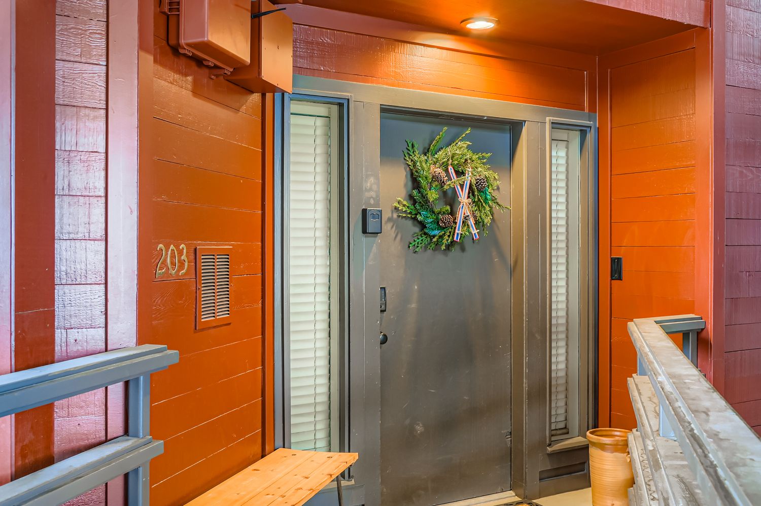 Modern entrance to unit 203 features a distinctive red wood exterior with contemporary glass door and seasonal wreath decor.