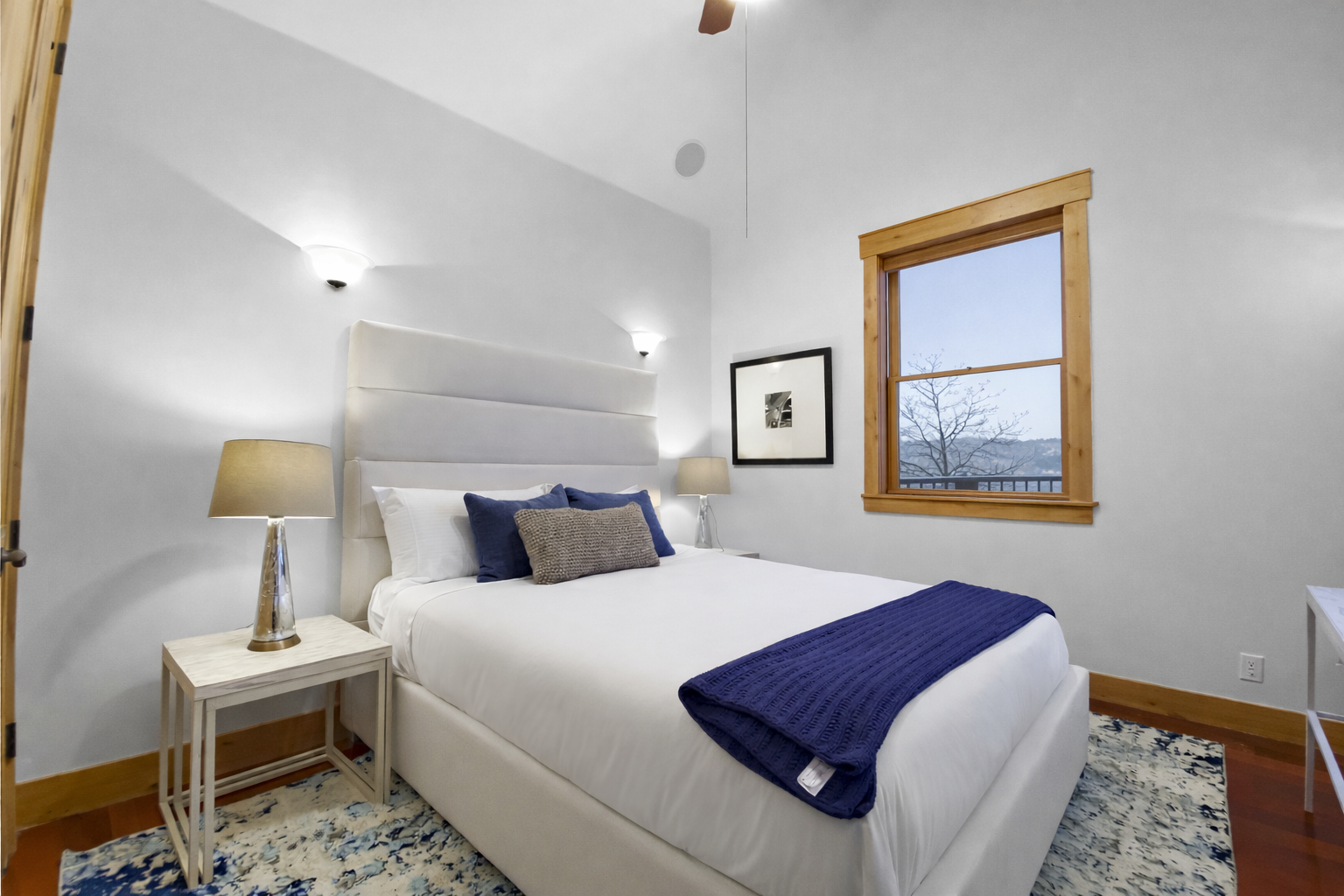 Drift off in your serene bedroom featuring crisp white linens with navy accents and peaceful mountain views through the wood-framed window.