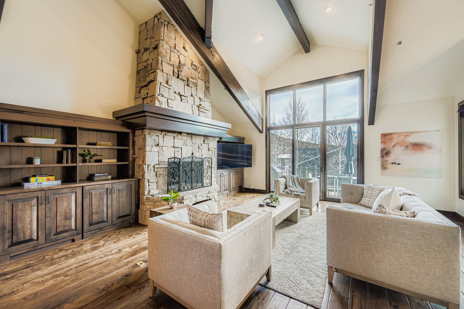 Unwind in your spacious living room featuring a stunning stone fireplace, cozy seating, and vaulted ceilings with exposed beams that create the perfect atmosphere for relaxation.