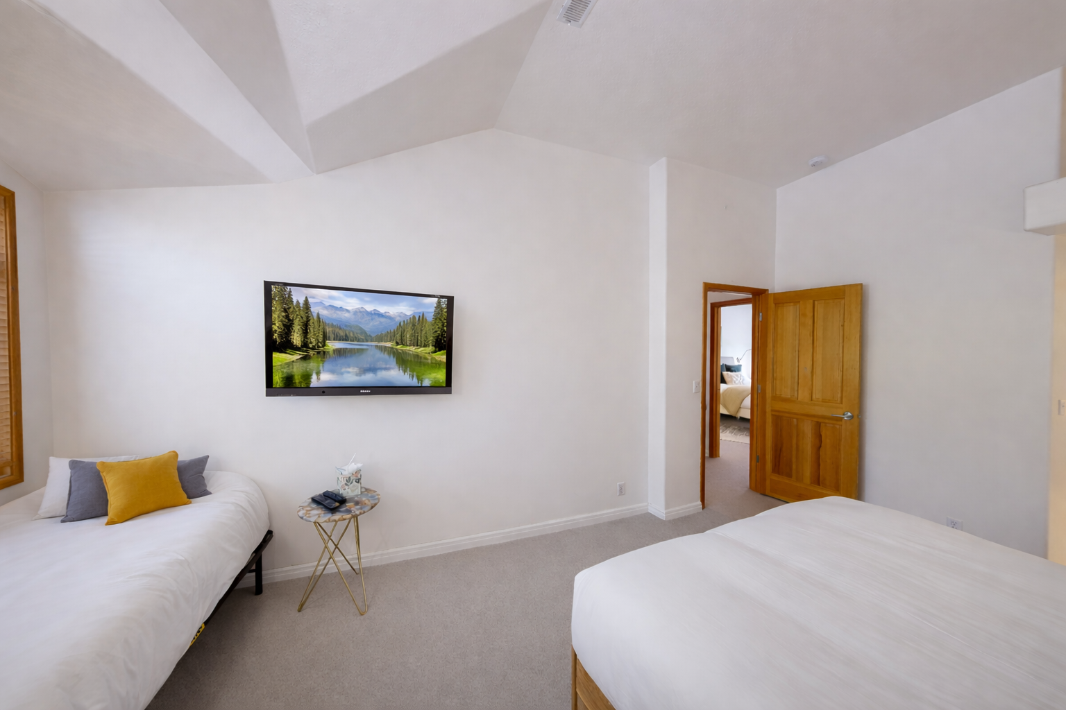Discover tranquility in this bright, minimalist bedroom featuring a comfortable natural wood bed and a cozy daybed. Large windows offer serene views of the outdoors.