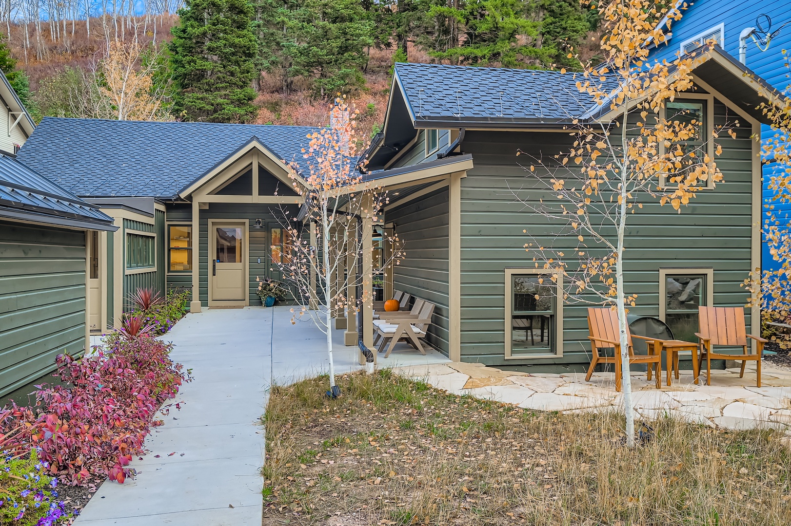 This charming mountain retreat features contemporary architecture with blue-green siding and inviting outdoor seating areas. The property is surrounded by aspens and evergreens, offering a peaceful autumn escape.