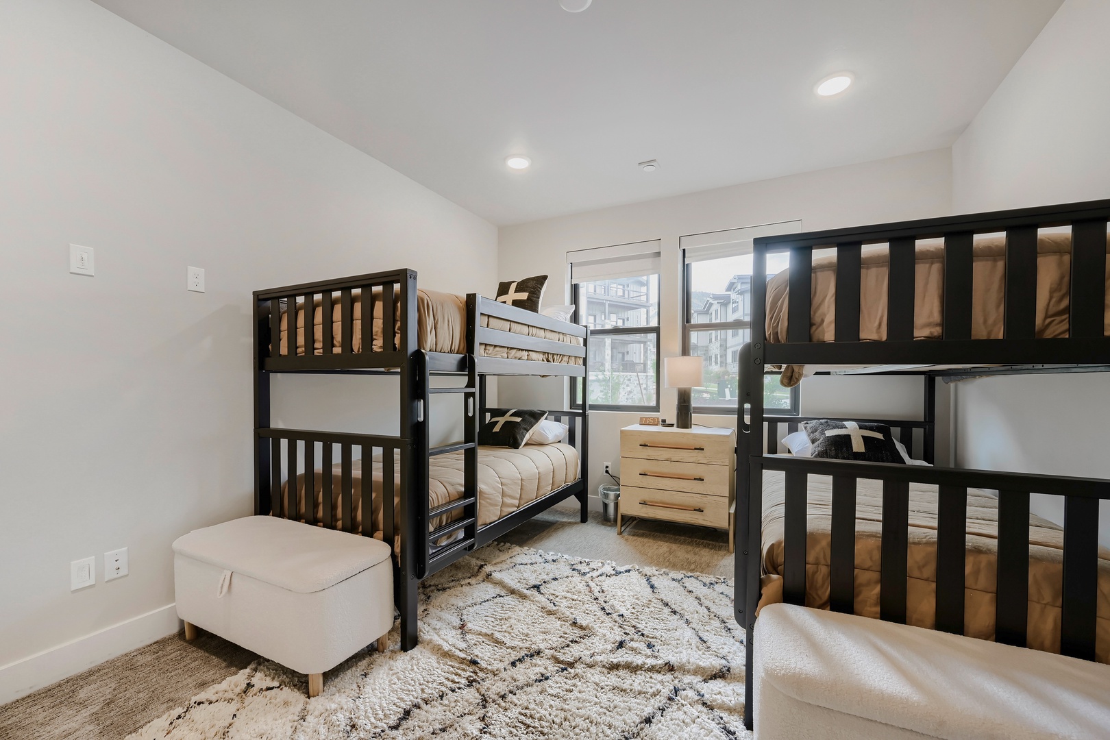 Bright, cozy bunk room with two sturdy bunk beds, plush ottomans, and soft rug. Ideal for families or groups seeking comfort and togetherness.