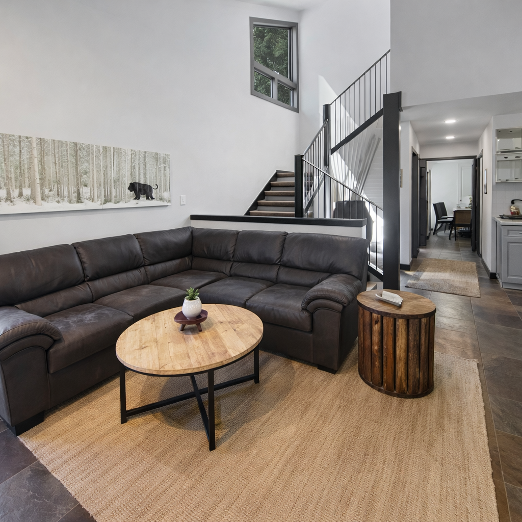 Cozy living room with a large sectional sofa, wooden floors, and easy access to the stairs and dining area. Your comfortable mountain basecamp.