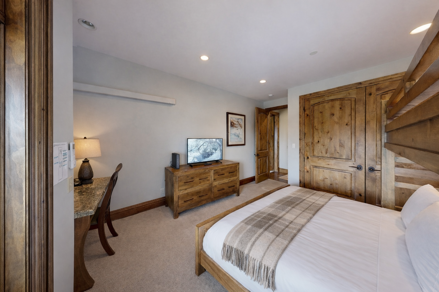 This versatile guest bedroom features a twin-over-queen bunk bed, perfect for families. Highlights include a dedicated workspace, large flat-screen TV, and ample storage, all in a bright, modern mountain setting.