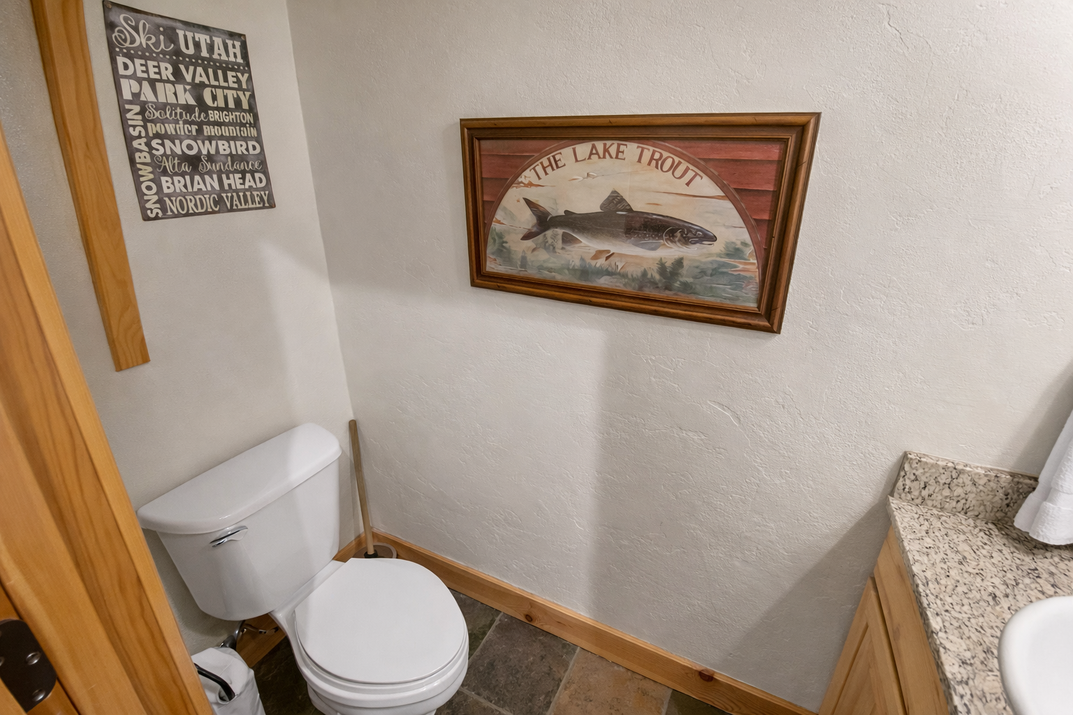 Step into a clean, functional powder room featuring wood flooring, a toilet, and rustic fish-themed art for a touch of cabin charm.