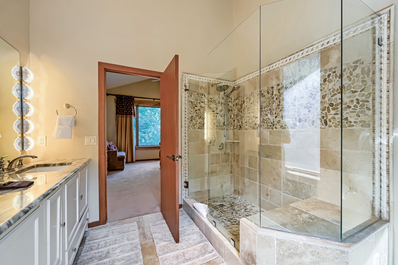 Step into your elegant en-suite bathroom, where warm natural light and sophisticated stone-accented tile create a spa-like retreat to refresh and unwind after your adventures.