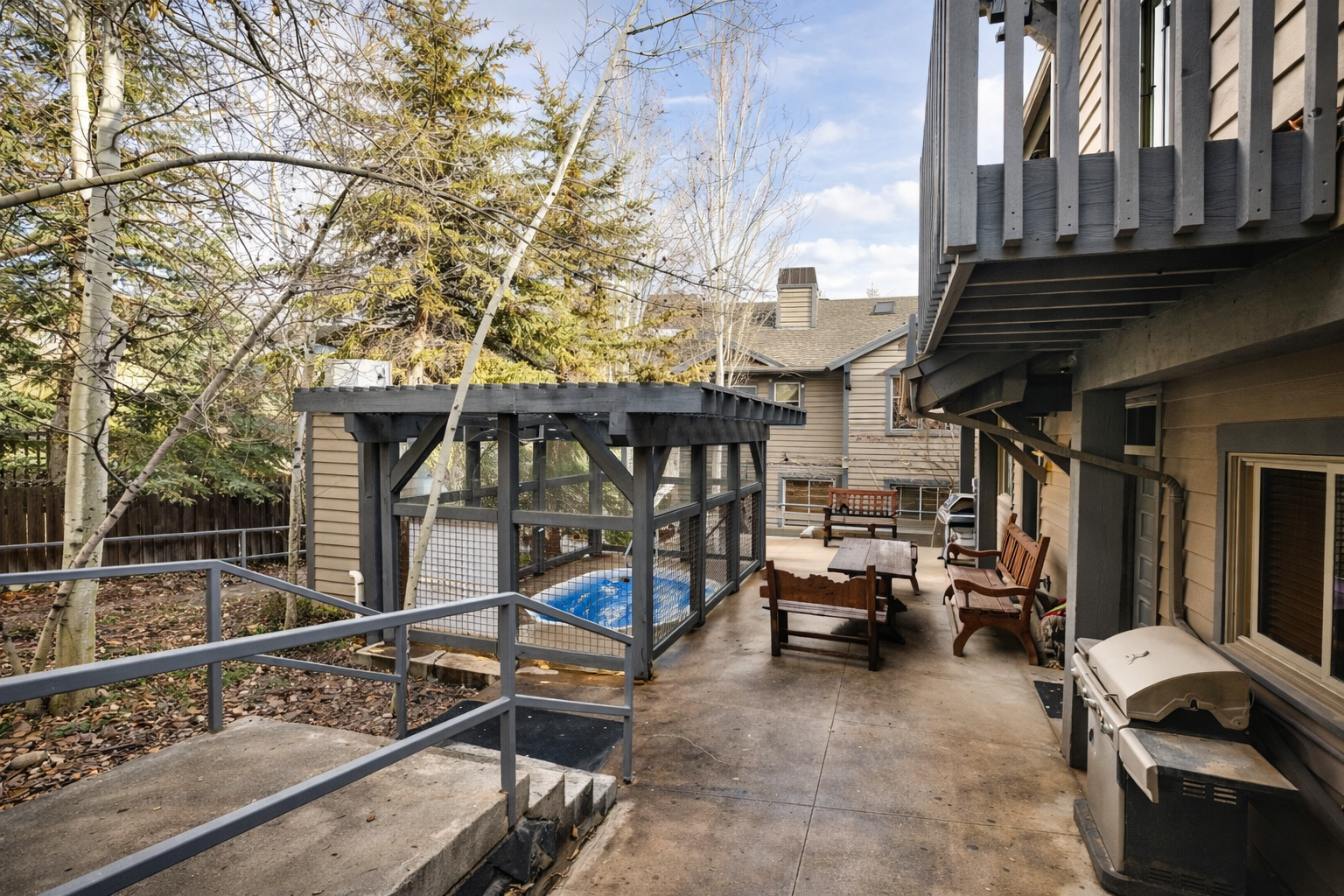 The property features a spacious concrete patio with comfortable seating and a gas grill, surrounded by aspen trees and evergreens in a peaceful neighborhood setting.