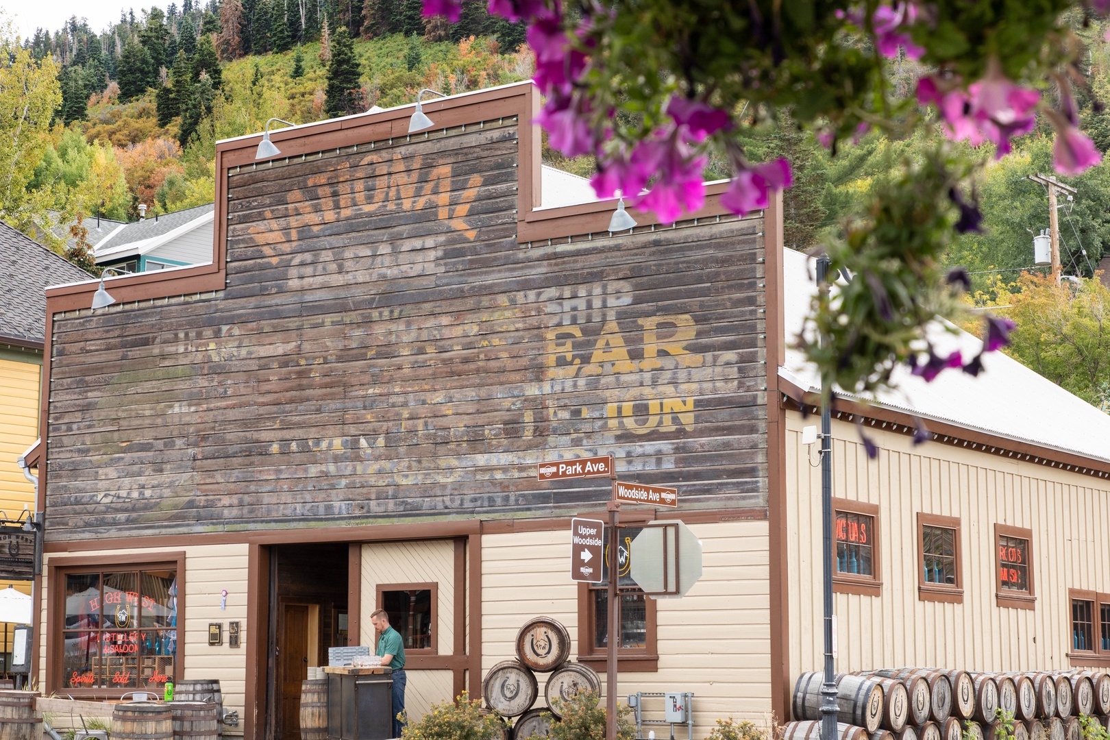 Historic building facade with weathered signage nestled among vibrant purple flowers and forested mountainside.