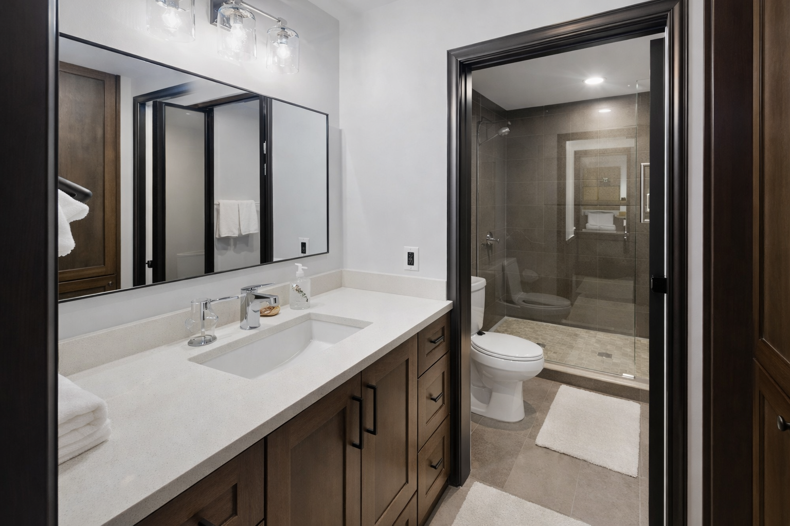 Step into your private spa-like bathroom featuring rich wood vanity, pristine white countertops, and luxurious walk-in shower with sleek glass enclosure.