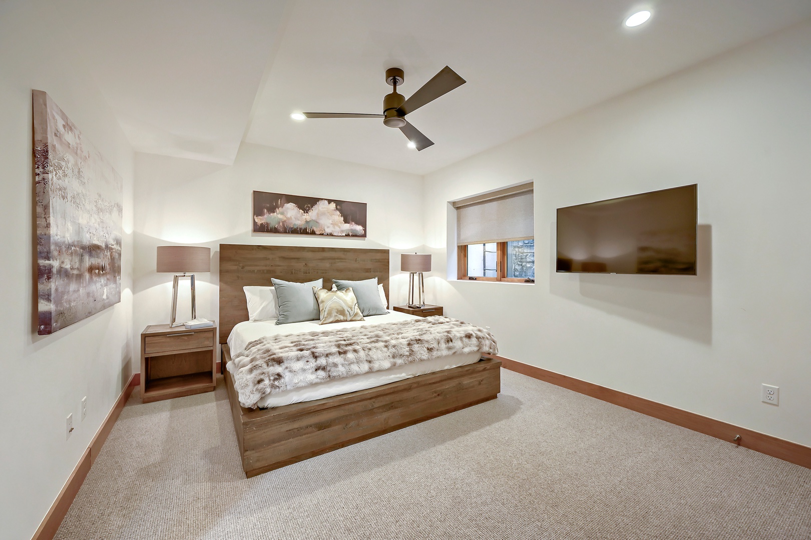 Unwind in your serene bedroom featuring a plush bed, warm wood accents, soothing art, and a modern ceiling fan for personalized comfort throughout your stay.