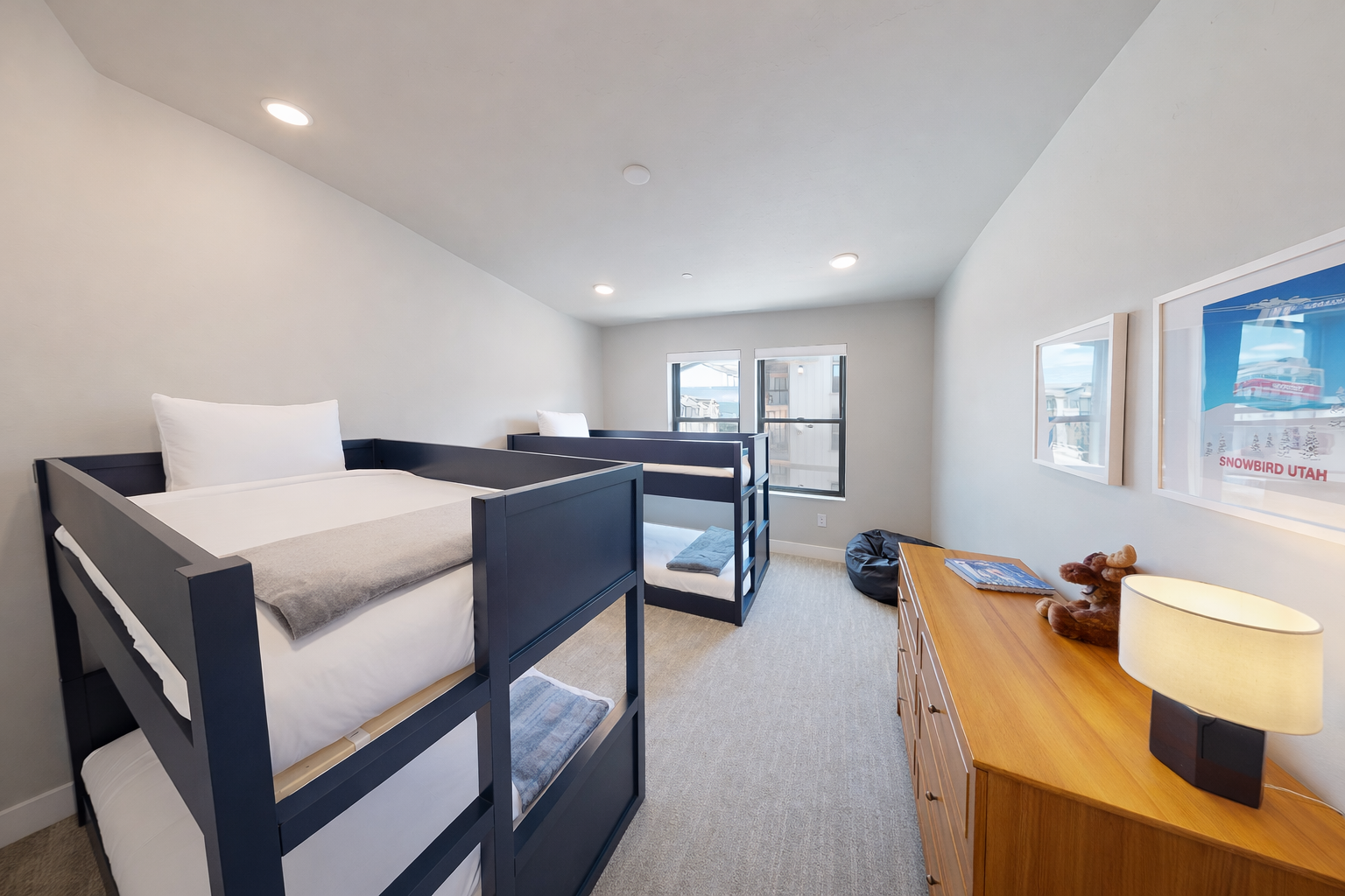 Perfect for kids or groups, this modern bunk room features sleek gray beds and a cozy blue gingham rug. Large windows offer bright, natural light and peaceful mountain views.