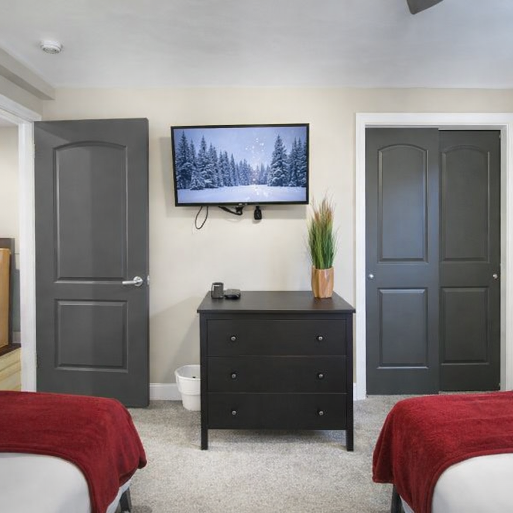 Cozy twin bedroom featuring plush beds with red throws, a snowy-scene smart TV, and soft lighting.