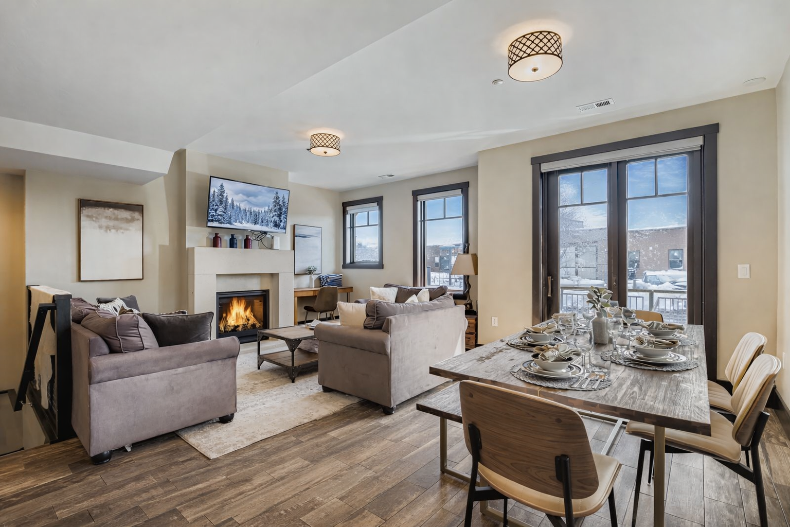 Relax in this light-filled open living area featuring a cozy gas fireplace, plush seating, and a large smart TV. Elegant wood flooring and contemporary finishes create a stylish, inviting mountain retreat.