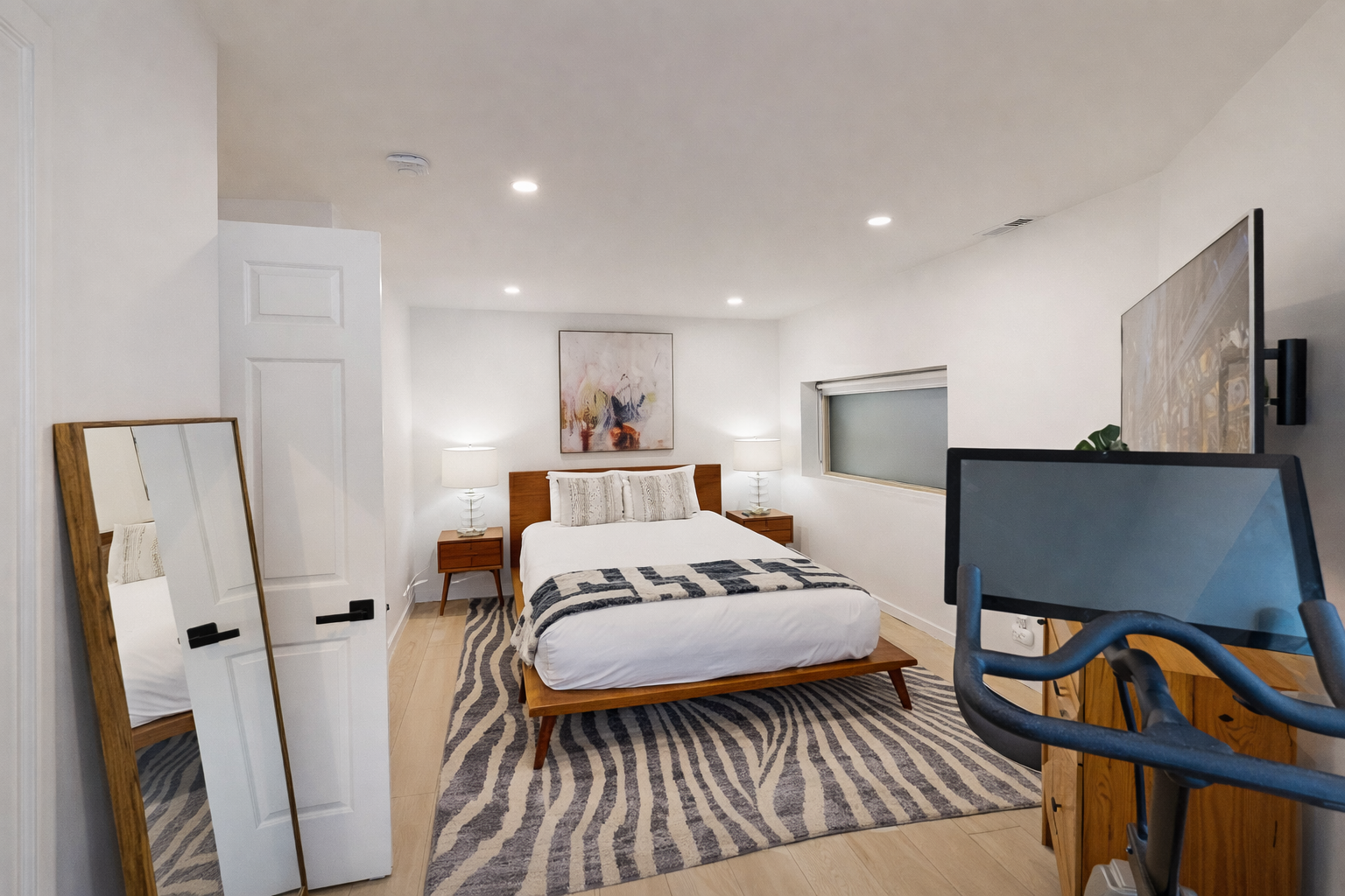 Relax in this serene, modern bedroom with a comfortable bed, ample storage, and a dedicated spin bike.