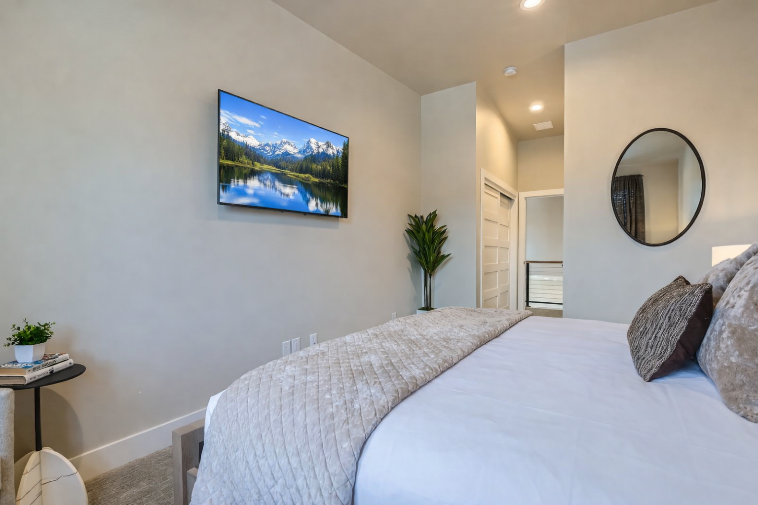 Unwind in your serene bedroom sanctuary with plush bedding, a large wall-mounted TV, and thoughtful touches like modern lighting and greenery.