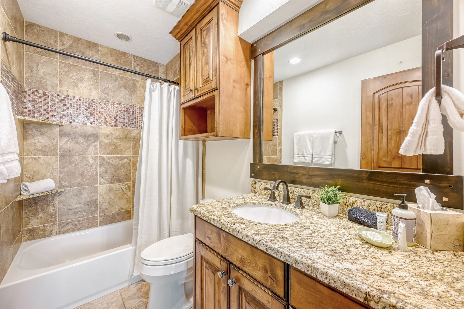 Unwind in your elegant bathroom featuring granite counters, warm wood cabinetry, and a relaxing tub-shower combo.