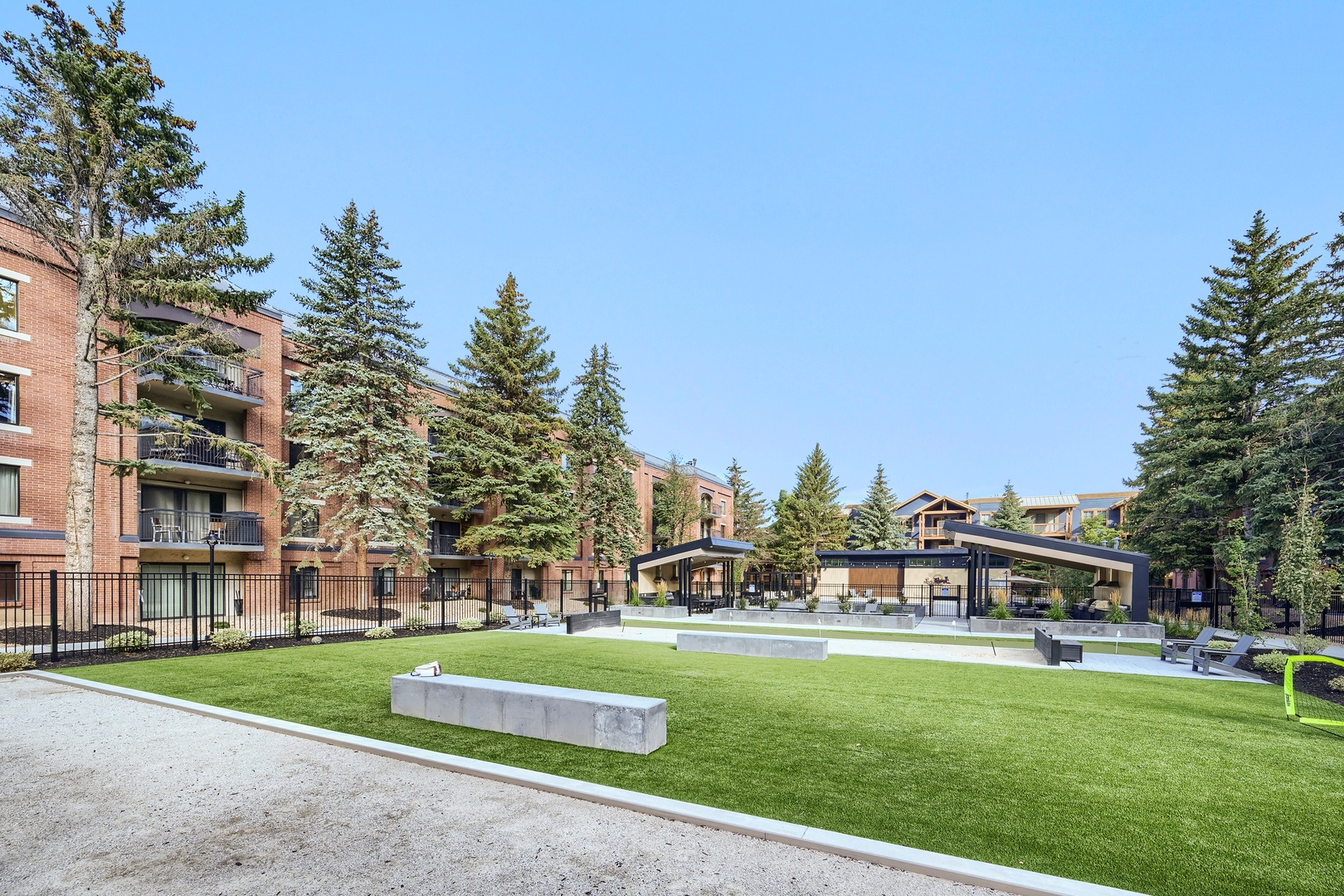 The property features an expansive common green space surrounded by tall evergreens and modern shared pavilions, creating a peaceful community atmosphere for outdoor gatherings and leisure.